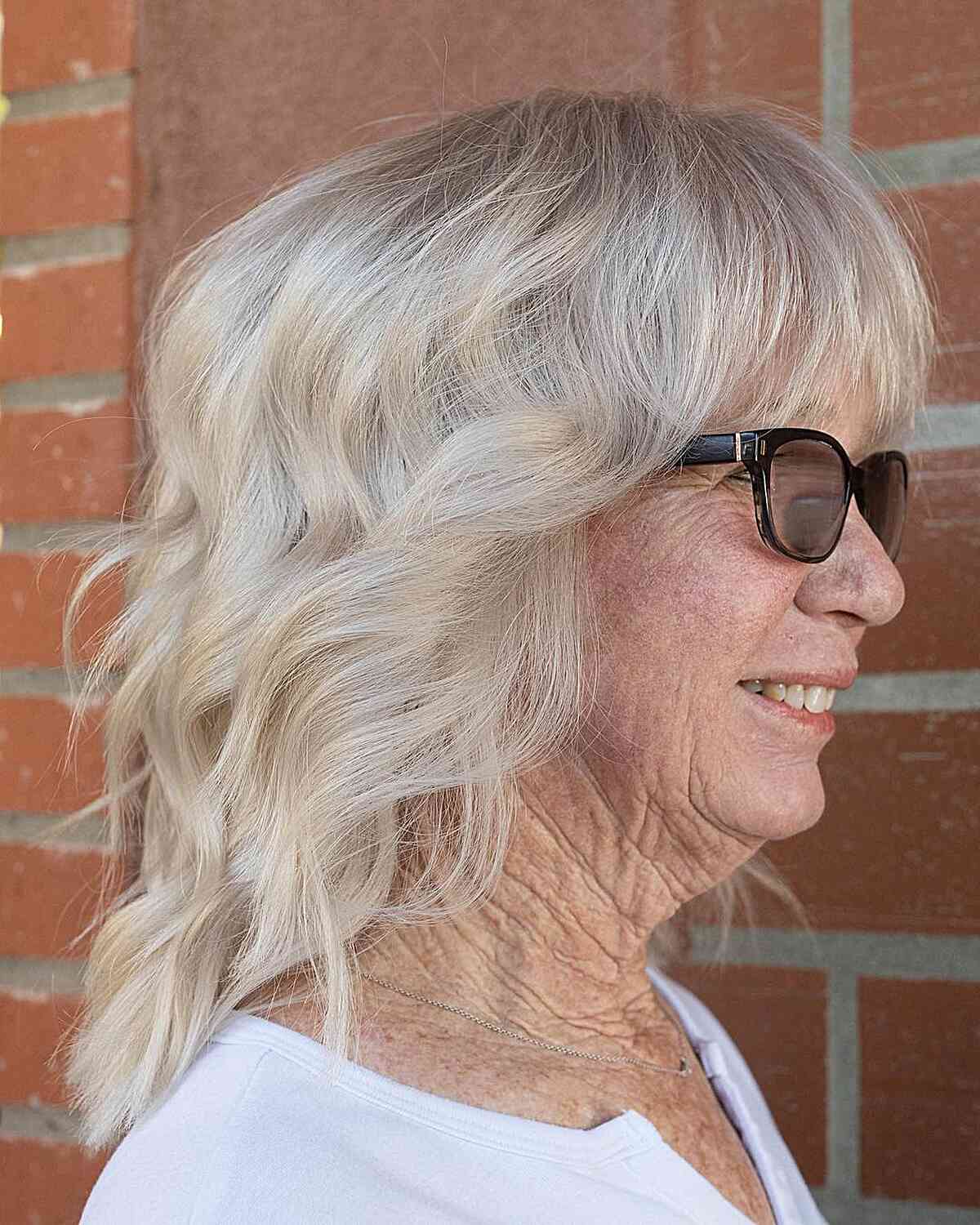 Uma espécie de penteado ondulado de platina de comprimento médio com um estrondo ondulado para avós com mais de 70 anos