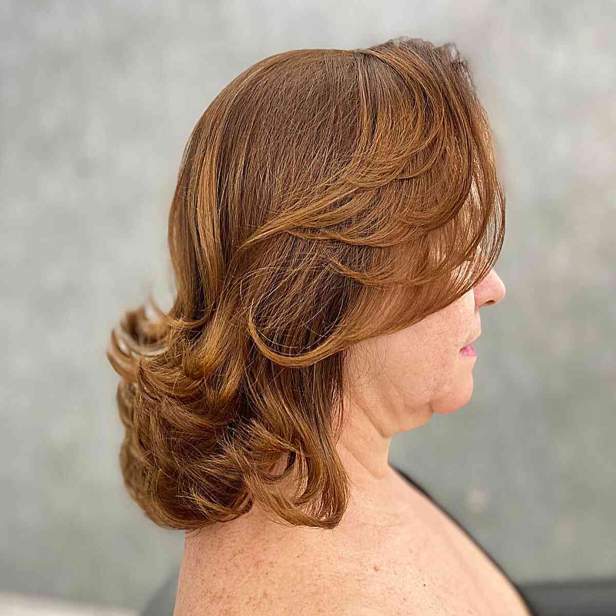 Cortes de cabelo com várias camadas com franja e pontas torcidas para mulheres completas aos 50 anos de idade com cabelo a ombros